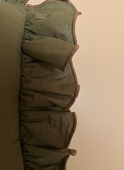 Close-up of a green 22x22 throw pillow with brown piping on a beige background