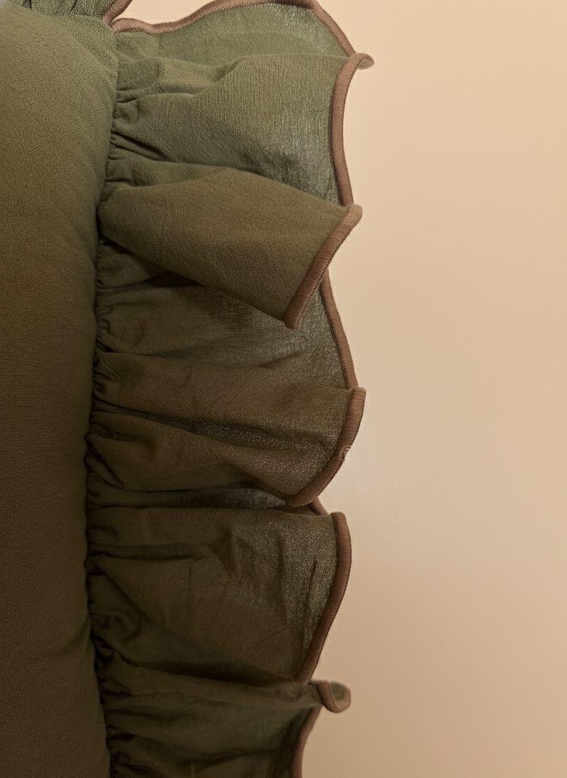 Close-up of a green 22x22 throw pillow with brown piping on a beige background